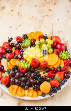 Plateau de fruits sains, Fraises Framboises Oranges Pommes Prunes Raisins kiwis mangues bleuets persimmon sur table en bois, de l'espace pour copier du texte, Banque D'Images