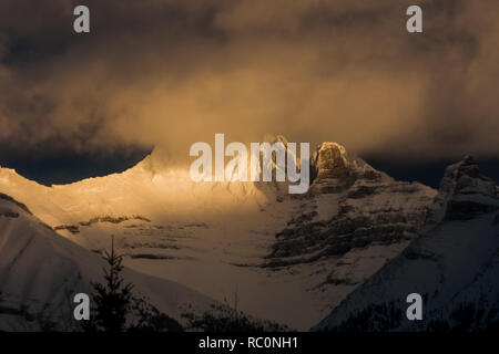 Coucher de soleil illumine la neige fraîche sur les sommets des montagnes dans le parc national de Banff, la création d'une lueur dorée, lors de belle journée d'hiver dans les Rocheuses canadiennes. Banque D'Images