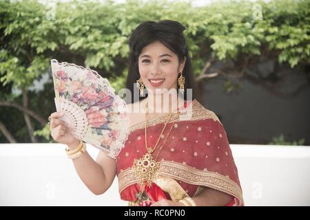 La jolie dame Thaï thaï traditionnel classique en milieu de séance habit de tenir un ventilateur est de poser dans un parc. Banque D'Images