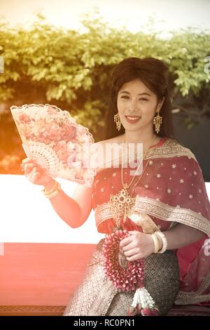 La jolie dame Thaï thaï traditionnel classique en milieu de séance habit de tenir un ventilateur est de poser dans un parc. Banque D'Images