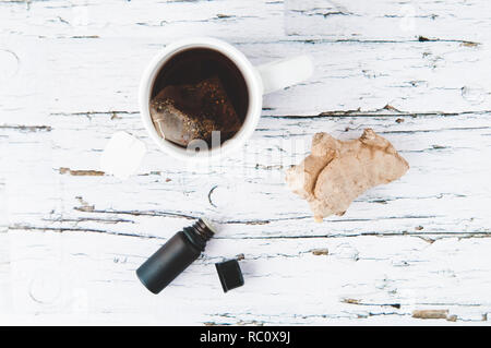 Bouteille d'huile essentielle, la racine de gingembre et d'une tasse de thé sur un fond de bois blanc Banque D'Images