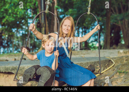 Mère et fils se balançant sur un vieux swing contre l'arrière-plan des racines de l'arbre Banque D'Images