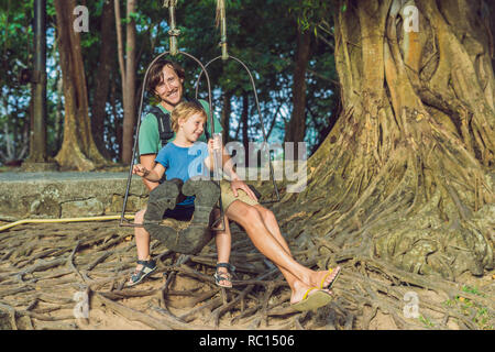 Père et fils se balançant sur un vieux swing contre l'arrière-plan des racines de l'arbre Banque D'Images