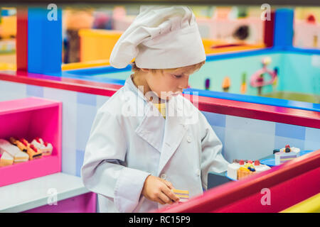 Le garçon joue le jeu comme s'il était un cuisinier ou un boulanger dans une cuisine pour enfants Banque D'Images