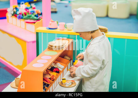 Le garçon joue le jeu comme s'il était un cuisinier ou un boulanger dans une cuisine pour enfants Banque D'Images