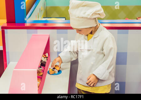 Le garçon joue le jeu comme s'il était un cuisinier ou un boulanger dans une cuisine pour enfants Banque D'Images