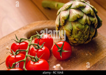 Tomates fermes et un artichaut sur une planche à découper en bois Banque D'Images