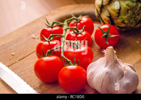 Les tomates, l'ail et les artichauts sur une planche à découper en bois. Banque D'Images