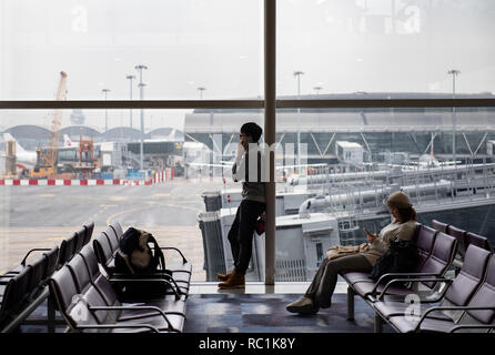 Les passagers assis dans la salle d'attente à la porte d'embarquement à l'Aéroport International de Hong Kong. Banque D'Images