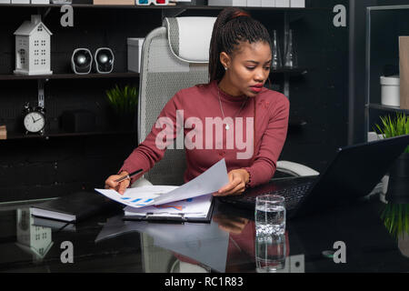 Portrait de jeune femme noire Utilisation des graphiques et diagrammes at Desk in office Banque D'Images