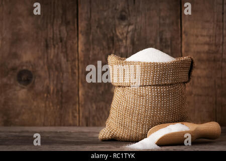 Sucre blanc en sac de toile et scoop sur fond de bois Banque D'Images