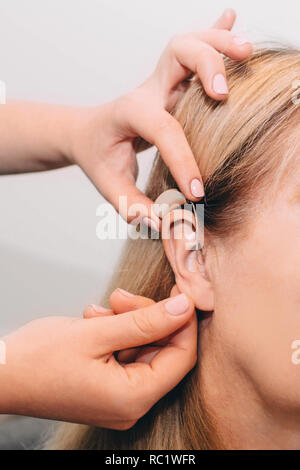 La main coupée de médecin l'ajustement d'aides auditives de l'oreille sur les femmes Banque D'Images