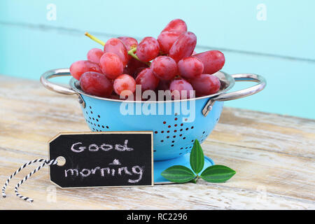 Bonjour carte avec des raisins rouges dans une passoire sur la surface en bois bleu Banque D'Images