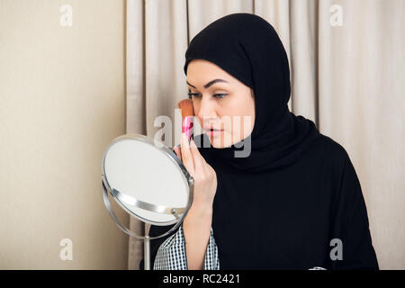 Beauté femme musulmane avec hijab appliquant le maquillage. Belle fille à la recherche dans le miroir et de l'application cosmétique. Fille obtient blush sur les pommettes. Banque D'Images