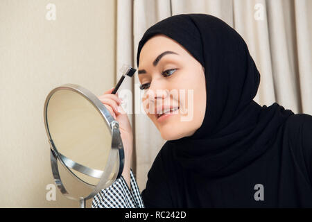 Une jeune femme musulmane façonner ses sourcils avec un pinceau Banque D'Images