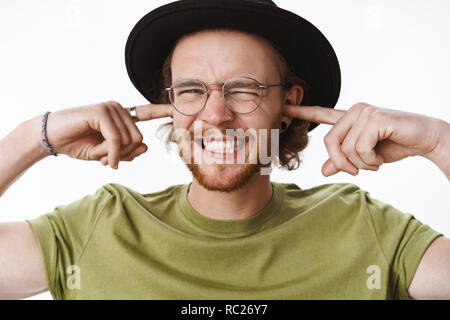 Guy fouines et serrer les dents comme le chant de clôture de l'audience amie mauvaise oreilles avec l'index d'être mécontent et irrité comme perturbé par le bruit terrible fort, posant la peine sur fond gris Banque D'Images