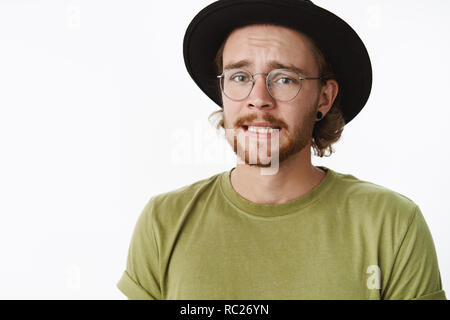 Aïe, je suis en difficulté. Portrait de inquiet triste mignon avec guy beard dans les verres et le serrement des dents, fronçant hat se sentir coupable que de mauvaise chose à l'ami(e) fond gris plus nerveux permanent Banque D'Images