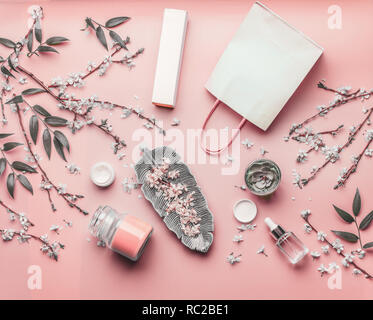 Concept esthétique. Divers produits pour le visage et papier panier sur fond rose pastel avec des feuilles et fleurs de cerisier, vue du dessus, cadre. Copy space Banque D'Images