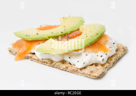 Un pain de seigle cracker propagation avec fromage cottage sans gras, tranches d'avocat et de poire, d'élevage des tranches de saumon fumé au poivre noir. Sur un fond blanc Banque D'Images