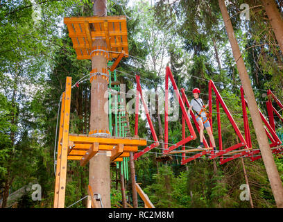 Adolescents passant hanging rope bridge obstacle à un parcours dans l'air extérieur parc aventure accrobranche Banque D'Images