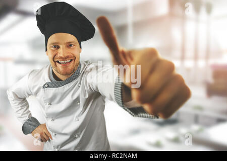 Young happy chef avec le pouce jusqu'à une cuisine de restaurant Banque D'Images