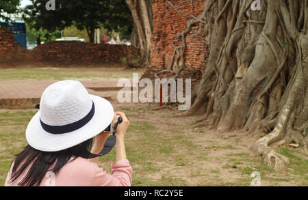 Woman Prendre des photos de la tête de Bouddha emprisonné dans les racines de l'arbre de Bodhi, Wat Mahathat Temple antique, le Parc historique d'Ayutthaya, Thaïlande Banque D'Images