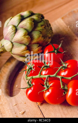 Tomates fermes et un artichaut sur une planche à découper en bois Banque D'Images