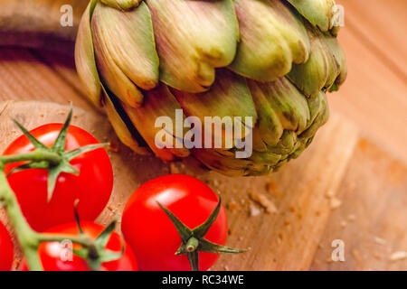 Tomates fermes et un artichaut sur une planche à découper en bois Banque D'Images