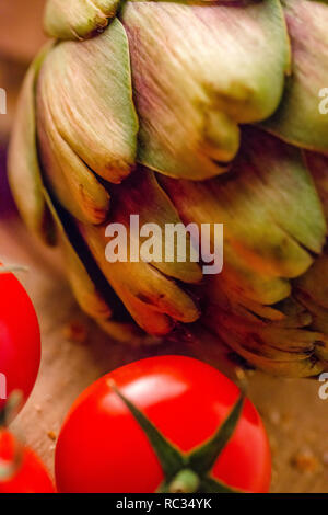 Tomates fermes et un artichaut sur une planche à découper en bois Banque D'Images