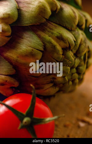 Tomates fermes et un artichaut sur une planche à découper en bois Banque D'Images