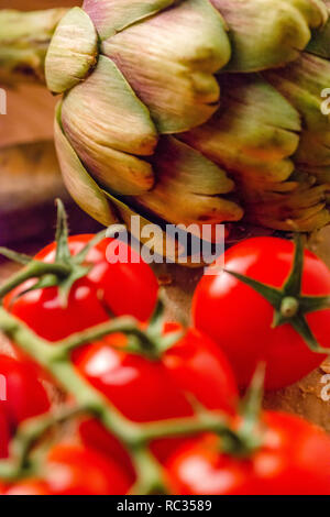 Tomates fermes et un artichaut sur une planche à découper en bois Banque D'Images