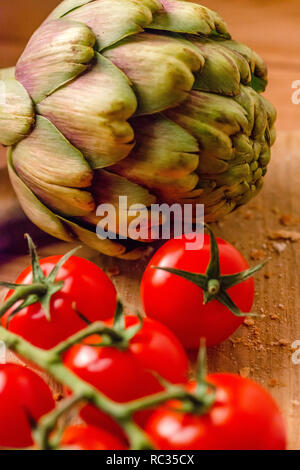 Tomates fermes et un artichaut sur une planche à découper en bois Banque D'Images