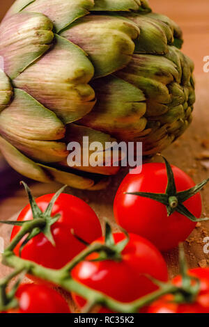 Tomates fermes et un artichaut sur une planche à découper en bois Banque D'Images