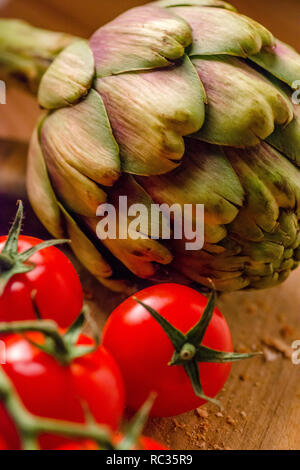 Tomates fermes et un artichaut sur une planche à découper en bois Banque D'Images