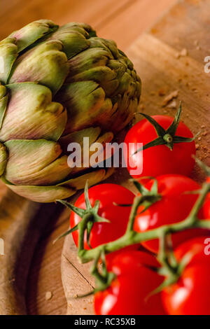 Tomates fermes et un artichaut sur une planche à découper en bois Banque D'Images