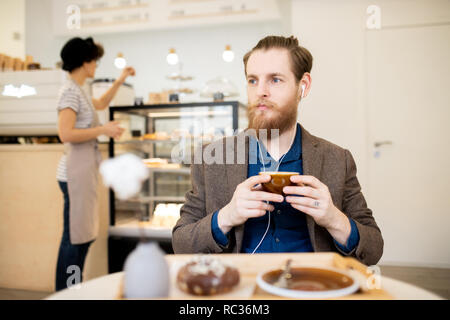 L'homme réfléchi des écouteurs de détente dans un café Banque D'Images