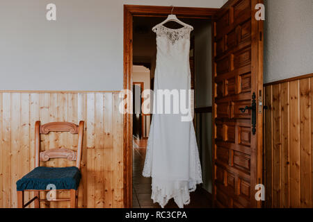 Une robe de mariée blanche accroché sur une porte en bois en plus d'une chaise dans une maison rustique Banque D'Images