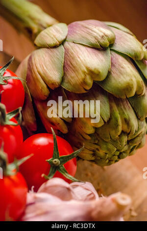 Les tomates, l'ail et les artichauts sur une planche à découper en bois. Banque D'Images