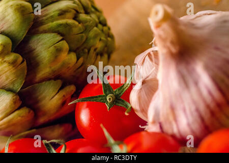 Les tomates, l'ail et les artichauts sur une planche à découper en bois. Banque D'Images