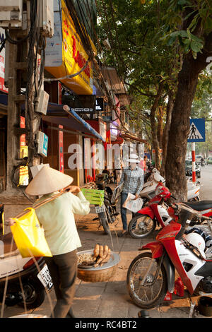 Vie quotidienne à Hanoi. Vendeur de rue avec des paniers et d'autres personnes marchant sur un trottoir étroit plein de scooters à l'ancien quartier de Hanoi, Vietnam. Banque D'Images