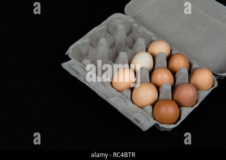 9 oeufs de poule dans une boîte en carton, isolé sur fond de feutre noir. Banque D'Images