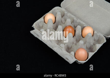 Quatre oeufs de poule dans une boîte en carton, isolé sur fond de feutre noir. Banque D'Images