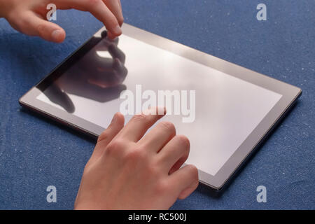 Utiliser les mains une pièce lumineuse tablette noir sur une feuille de tissu bleu. Banque D'Images