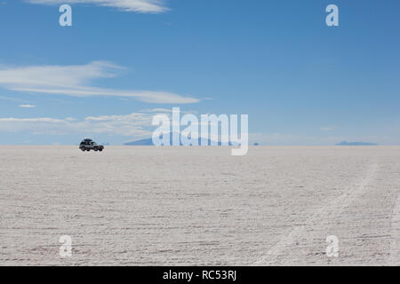 Un 4x4 traversant les salines d'Uyuni près de l'Île Incahuasi est éclipsé par l'incroyable et vaste paysage blanc. Banque D'Images