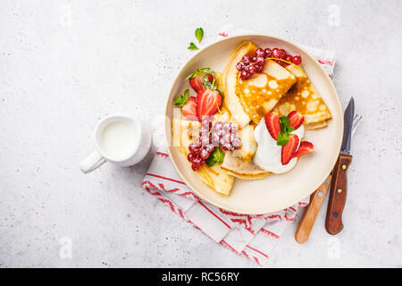 Des crêpes fines crème caillé, groseilles, fraises et du sucre en poudre en plaque blanche. Petit-déjeuner sain beau concept. Banque D'Images
