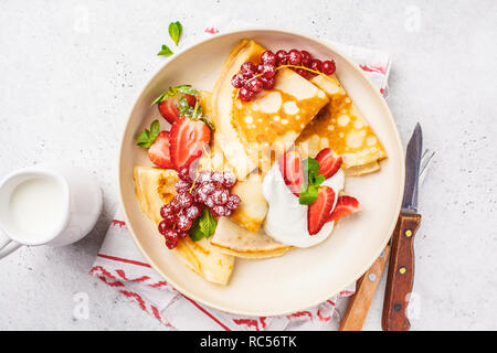 Des crêpes fines crème caillé, groseilles, fraises et du sucre en poudre en plaque blanche. Petit-déjeuner sain beau concept. Banque D'Images