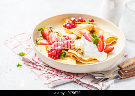 Des crêpes fines crème caillé, groseilles, fraises et du sucre en poudre en plaque blanche. Petit-déjeuner sain beau concept. Banque D'Images