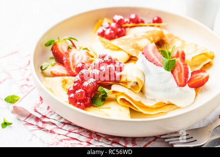 Des crêpes fines crème caillé, groseilles, fraises et du sucre en poudre en plaque blanche. Petit-déjeuner sain beau concept. Banque D'Images