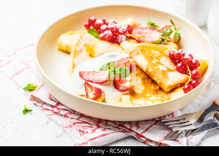 Des crêpes fines crème caillé, groseilles, fraises et du sucre en poudre en plaque blanche. Petit-déjeuner sain beau concept. Banque D'Images