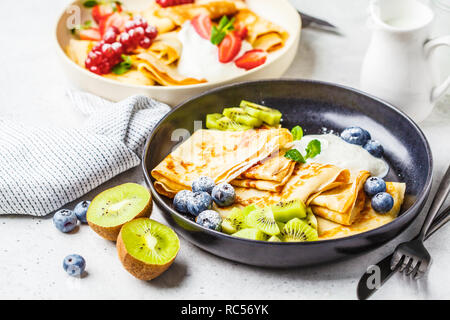 Crêpes minces faits maison servis avec crème de fromage, fruits et baies en noir et blanc des plaques. Petit-déjeuner sain beau concept. Banque D'Images